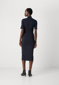 Navy ribbed midi dress with short sleeves, high neck, and fitted silhouette, paired with black ankle boots. Smooth texture, minimal design.