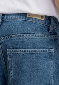 Vaqueros de denim en azul claro con un acabado texturizado. Cuenta con una etiqueta estampada "EST. 1992" cerca de la cinturilla y costuras de contraste.
