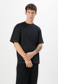 Zwarte katoenen t-shirt met een ontwerp met korte mouwen, ronde hals, voorzak en contrasterende witte stiksels.