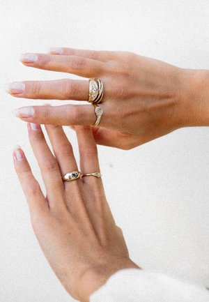 Gold rings on two hands; one hand displays three rings with various designs, including a marquise shape and a simple round ring.
