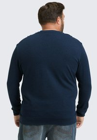 Marineblauer Langarmpullover aus strukturiertem Stoff mit gerippten Bündchen und Saum sowie einem klassischen Rundhalsausschnitt. Getragen mit Denim-Jeans.