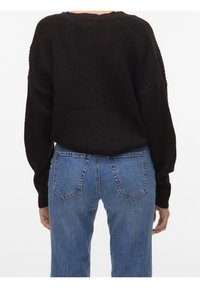 Brązowy sweter dziany o luźnym kroju, z szerokimi rękawami i teksturowanym wzorem, zestawiony z wysokim stanem niebieskich jeansów.