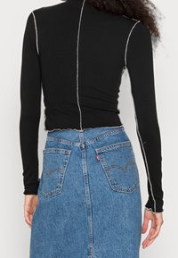 Svart långärmad topp med kontrasterande vit sömnad, kort design och vågig fåll, tillsammans med en högmidjad jeanskjol.