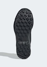 Suela de zapato atlético negra con una superficie texturizada que presenta un patrón de tracción hexagonal y acentos curvados, diseñada para agarre y estabilidad.