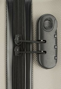 Schwarzer Reißverschluss mit doppelten Zippern auf einem strukturierten silbernen Stoffkoffer, ausgestattet mit einem schwarzen Zahlenschloss und einem ergonomischen Griff in der Nähe des Reißverschlusses.