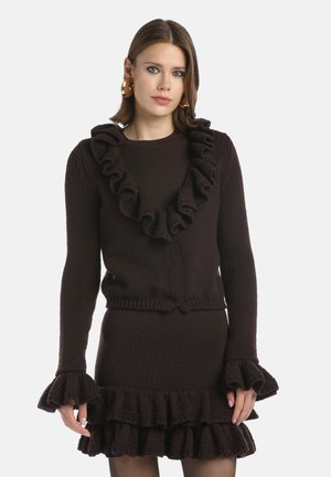 Kötött sötétbarna pulóver fodros nyakkivágással és mandzsettákkal, hozzá illő fodros szoknyával párosítva. Ismert formázott dizájn texturált anyagból.