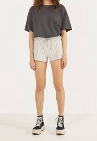 Grå bomullströja med korta ärmar, parat med grå shorts med dragsko. Modellen bär svarta högskurna sneakers med vita sulor och snören.