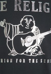 Svart t-shirt med en silvergrafik av en leende figur som spelar gitarr, med texten "MODE FÖR SINNEN" nedanför.