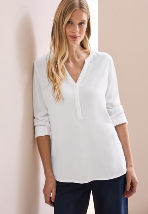 Weiße Bluse mit langen Ärmeln, V-Ausschnitt und Knopfleiste. Verfügt über umgeschlagene Manschetten und einen leicht abgerundeten Saum, dargestellt vor einem hellen Hintergrund.