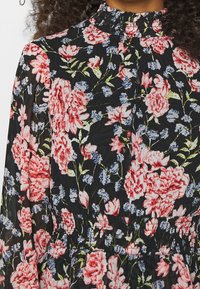 Blommig blus med svart bakgrund och stora rosa och blå blommor, hög krage med rynkad textur, och resårmidja.