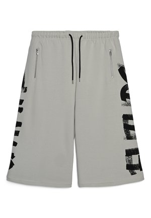 Pantaloncini grigio chiaro in tessuto morbido, con un disegno grafico nero sul lato sinistro e due tasche con zip sul davanti.