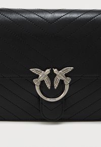 Mustmust nahkakott, millel on chevroni tikandi muster, ringikujuline hõbedane klamber, mis on kaunistatud kahe linnu aktsendiga ja logoga.