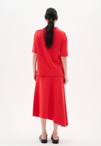 Rode twee-delige outfit bestaande uit een top met korte mouwen en een enkellange rok met een vloeiende design. Matte stof en een eenvoudige silhoeet.