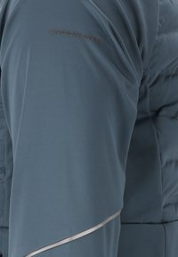 Blåt stof med "ENDURANCE" tekst og polstret materiale synlig, hvilket antyder design detaljer til sportstøj eller overtøj.