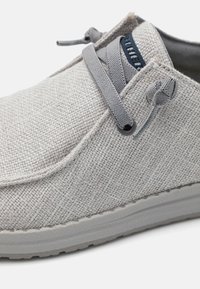Ljusgrå tygsko med strukturerad yta, rund tå och grå snörning. Elastiska sidor för passform, kontrasterande blå logotyp på tungan.