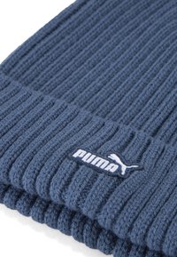 Gorro de punto azul oscuro con textura acanalada, con un parche de logo de Puma blanco en la parte frontal. Material suave y grueso.