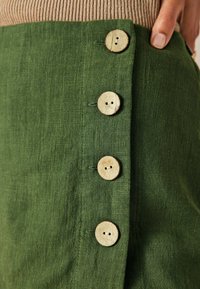 Grön linnekjol med fyra träknappar längs sidan, som visar en strukturerad yta och en ren, enkel design.