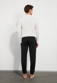White long-sleeve top with a smooth texture paired with black, slim-fit pants featuring cuffed ankles. No visible patterns or hardware.