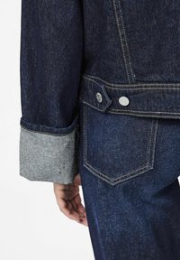 Jean jacket, joka sisältää tummansinisen rungon, harmaat hihat ja hopeiset napit. Tekstuuri on sileä ja klassinen muotoilu, jota korostavat kontrastivärit.
