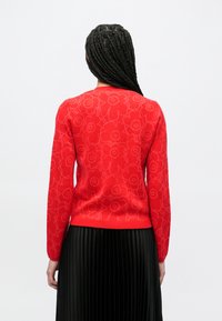 Rode trui met bloemenmotief en lange mouwen, gemaakt van zacht gebreid materiaal. Het gestructureerde bloemmotief contrasteert met het gladde lichaam.