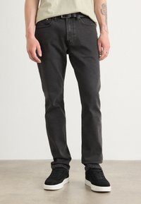 Zwarte denim jeans met een slim fit, voorzien van vijf zakken, een klassieke gulp en subtiele stiksels. Gecombineerd met zwarte sneakers.