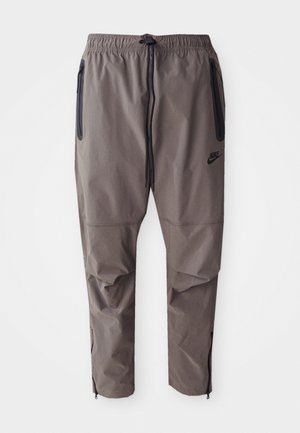 Gray Nike pants with an elastic waistband, drawstring, side zippered pockets, and zippers at the ankles for adjustable fit.