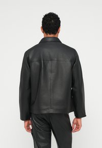 Chaqueta de cuero negro con una textura suave, corte relajado y un cuello afilado. Presenta una costura en el yugo trasero y mangas rectas.