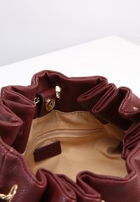 Burgundowa skórzana torebka wnętrze z falbaniastym wykończeniem, złotymi akcesoriami i jedną kieszonką na zamek umieszczoną na beżowej podszewce.