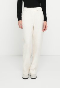 Világos színű, texturált, bőszár�ú nadrág sima derékpánttal, elülső zsebekkel és egyenes sziluettel. Szürke cipővel viselve.