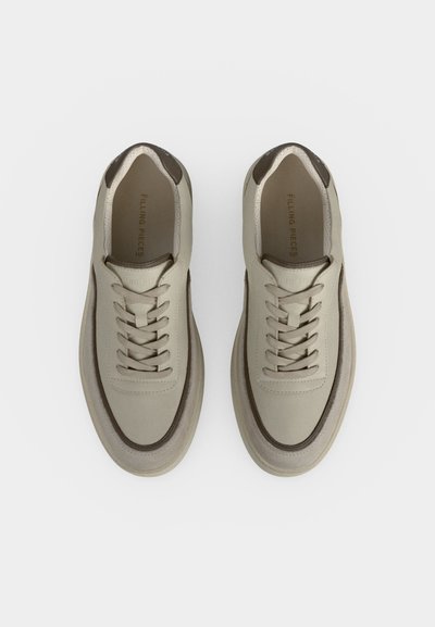 Paire de baskets en cuir beige à lacets avec bordure marron et semelles rembourrées vues de dessus sur fond blanc.