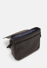 Bolso de hombro de cuadros marrones con una textura suave. Parte superior abierta que revela un interior azul marino, cuenta con un cierre de solapa y una correa ajustable.