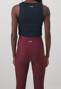 Marinblå kort ärmad tank top med rund halsringning; kombinerat med högmidjade vinröda leggings med en logotyp vid midjan. Slät, stretchig tyg.