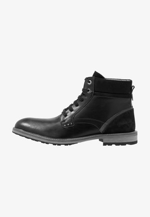 Black leather and suede ankle boot with lace-up closure, textured finish, metal eyelets, and star accents on the side. Rubber sole.