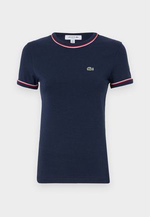 Mørkeblå bomulls T-skjorte med korte ermer, rød og hvit stripete kanting ved kragen og ermene, med en grønn brodert logo på brystet.