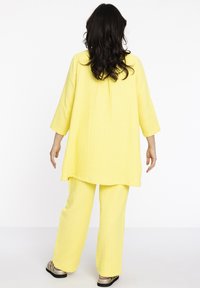 Geel twee-delige outfit bestaande uit een losse tuniek met lange mouwen en bijpassende broek. Gestructureerde stof met een gekreukt ontwerp, comfortabele pasvorm.