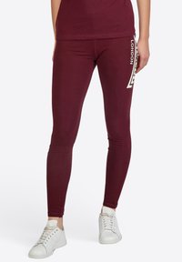 Bordeauxfarbene Leggings mit einer schmalen Passform und glatter Textur. Sie verfügen über einen weißen "LONDON"-Druck und geometrische Muster an der Seite.