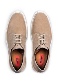 Scarpe in suede beige con suola in gomma bianca, punta rotonda e lacci grigi. L'interno presenta una fodera marrone e un'etichetta del marchio rossa.