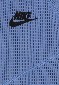 Blue mesh fabric with small, evenly spaced holes. Features black Nike logo and visible stitching along edges.