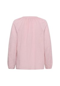 Blouse rose clair à manches longues avec le haut du dos froncé et des motifs floraux brodés subtils sur les manches et le tissu.