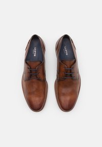 Zapatos de vestir de cuero marrón con un acabado suave, punta redonda, diseño de cordones y costura en contraste. Logo visible en la plantilla.
