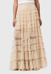 Μπεζ φούστα σε επίπεδα, φτιαγμένη από διαφανές ύφασμα με ρυτιδωτά στρώματα. Διαθέτει ελαστική μέση και απαλή υφή, σχεδιασμένη για ροή και κίνηση.