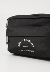 Juodas nailono kosmetikos krepšys su dviem užtrauktukais, su baltu spausdintu tekstu "Karl Lagerfeld Paris" ir "21 Rue St-Guillaume."