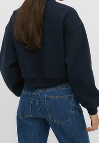 Navyblauwe cropped sweatshirt met een ronde hals, ribbelzoom en verlaagde schouders, gecombineerd met hooggeplaatste blauwe denim jeans met achterzakken.