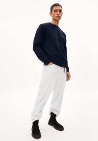 Marineblauwe sweatshirt met ronde hals, gedragen met lichtblauwe, loszittende broek en zwarte enkellaarzen. Eenvoudig ontwerp, gladde textuur en relaxte pasvorm.