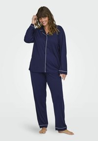 Navyblå pyjamasset i mjukt tyg, med en skjortkrage med vita detaljer och långa ärmar, matchat med löst sittande byxor.