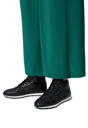 Des baskets montantes noires présentent un dessus en cuir texturé, des lacets ronds et une semelle en caoutchouc blanche. Associées à un tissu vert fluide.