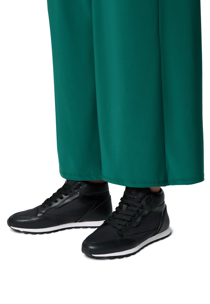Zapatillas altas negras cuentan con un upper de cuero texturizado, cordones redondos y una suela de goma blanca. Combinadas con una tela verde fluida.