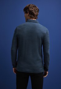 Dlouhý rukáv, tmavě modrá polo košile se strukturovaným designem, s klasickým límečkem a zakřiveným lemem. Nosí se s černými kalhotami.