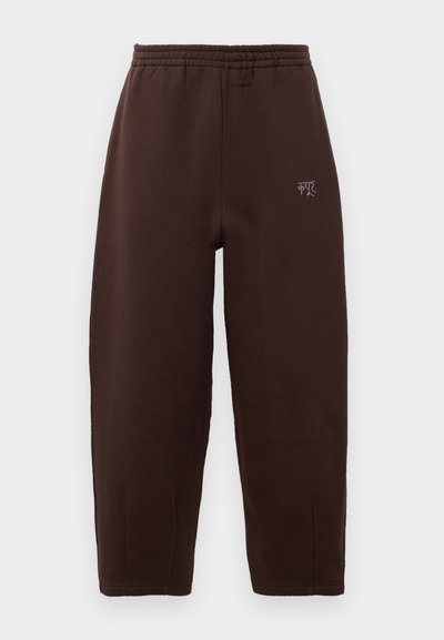 Brown cotton sweatpants with an elastic waistband, tapered legs, and a small logo accent on the left side. Soft texture, minimal design.