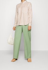 Camicia a righe bianca e rosa pallido, con due tasche sul petto; abbinata a pantaloni a gamba larga verde chiaro. Accessoriata con una borsa bianca e sandali color nocciola.